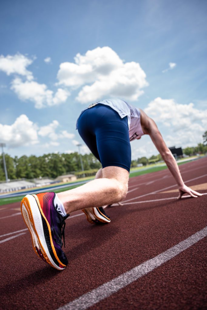 An athlete is in position in his running block to run. He wears csu sports clothes