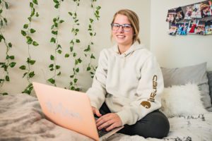A grirl woth her computer on her bed with pictures and decoration on the wall