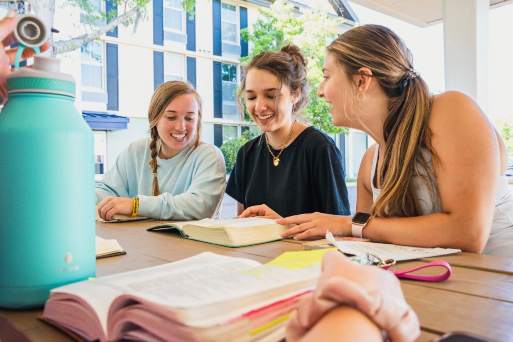 Three girls sitting outside at a table reading the Bible