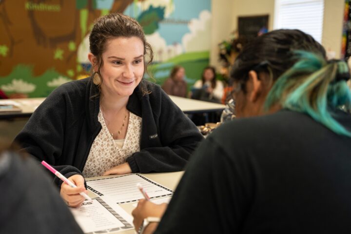 Two women with a pen and paper and talking to each other