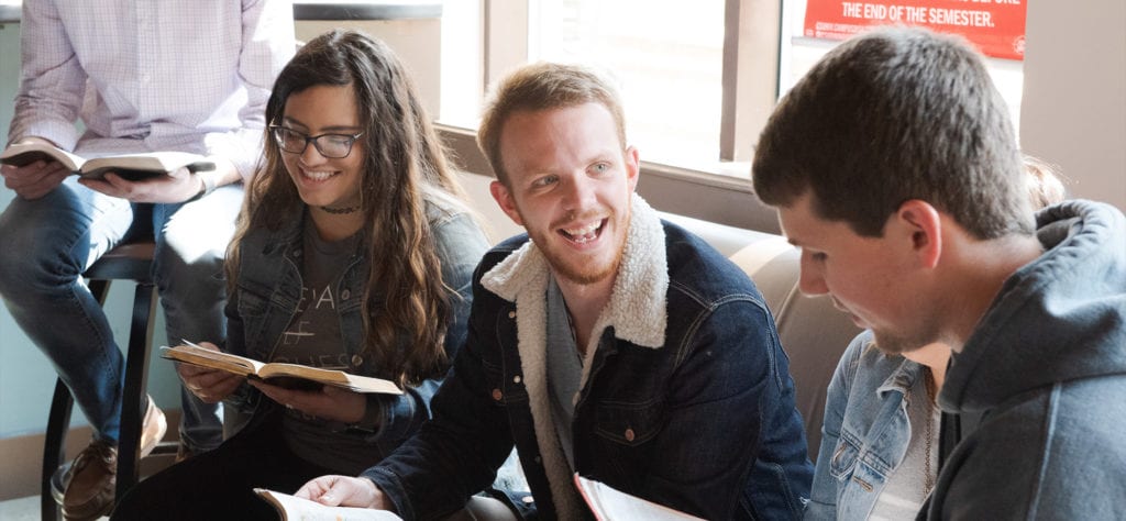 Students with Bibles, sitting in Java City at CSU, talking with each other.