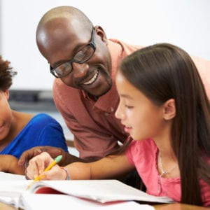 Teacher helping an elementary student who is writing in her notebook.