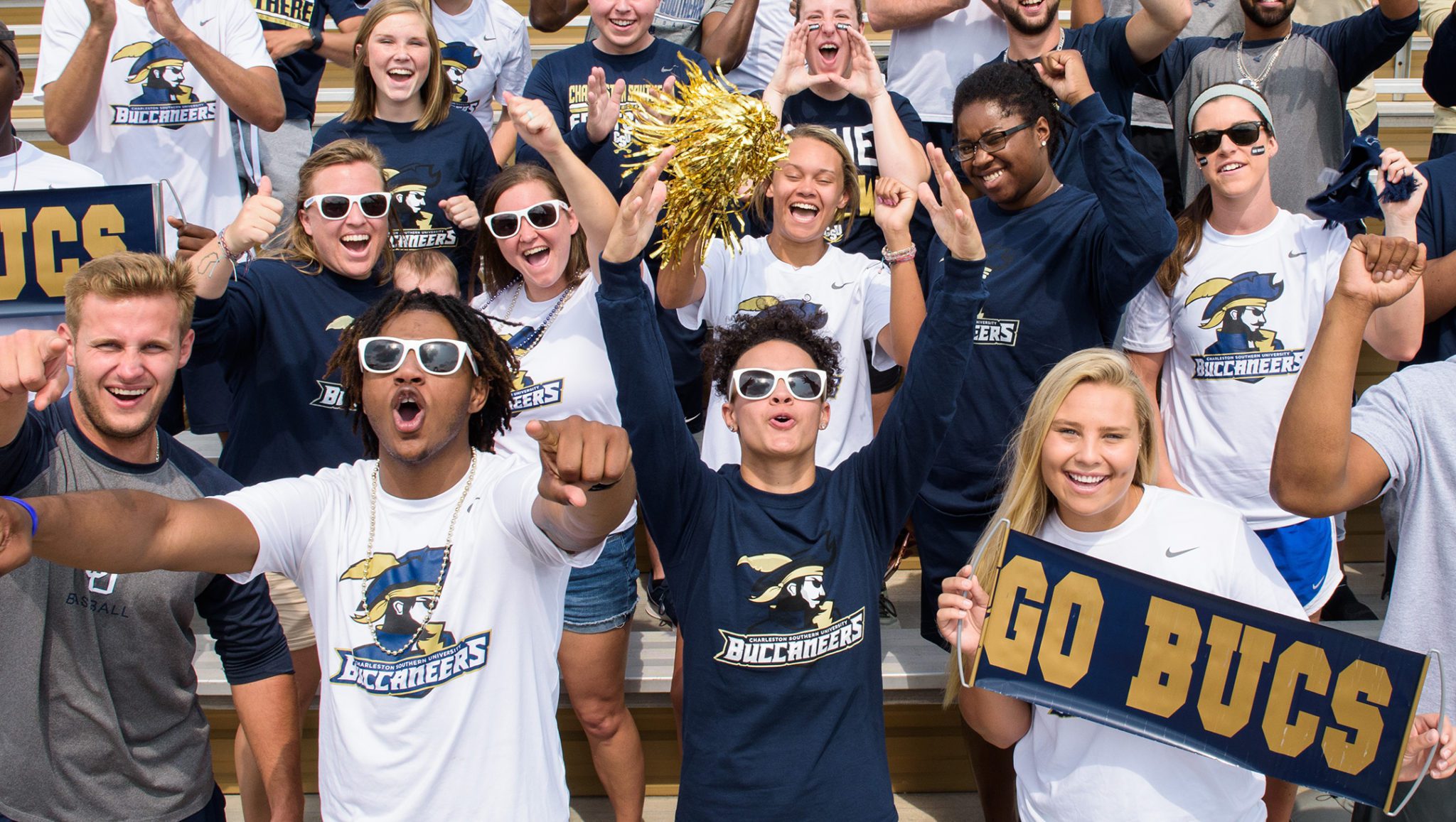 Student-athletes cheering in the stands of the football stadium at CSU. Everyone is wearing a Buccaneers shirt and some have Go Bucs signs.