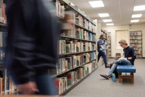A student sitting on a bench near the book racks in the Rivers Library at CSU