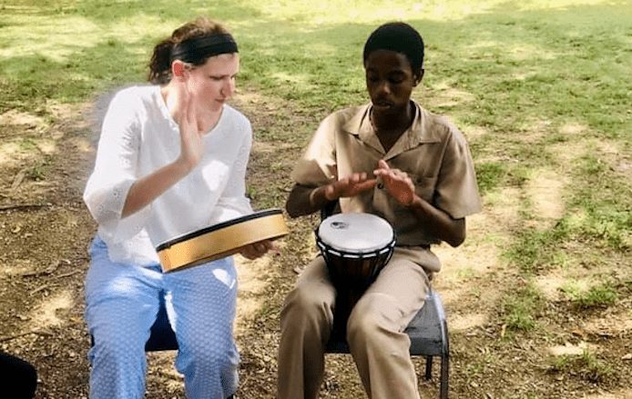 Melinda Gorsky studying abroad in Jamaica, playing bongo and tambourine with a young boy.