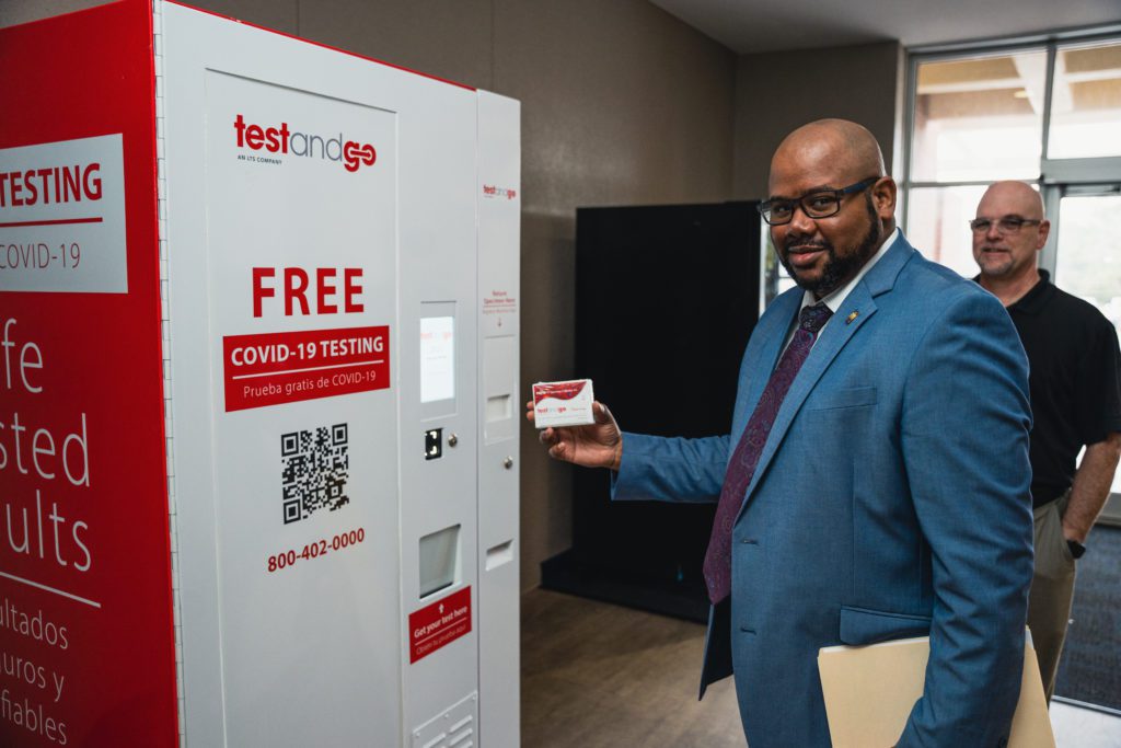 A man shows the self-diagnostic covid box in his hand with the machine in front of him