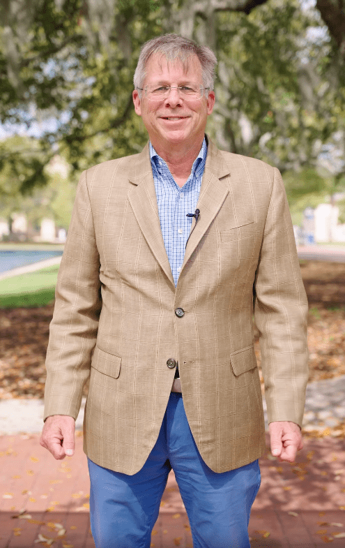 Male CSU professor in sport coat and blue jeans stands on brick walkway talking to the camera