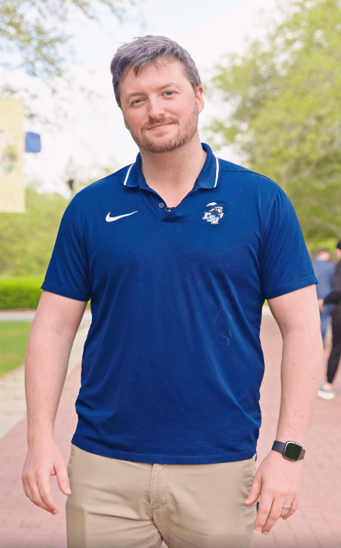 White male student in navy CSU polo faces the camera standing on a brick walkway