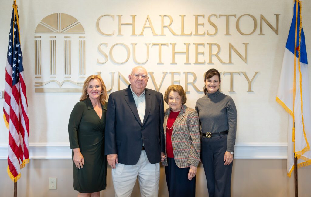 Four people taking a picture between two flags and CSU in the background