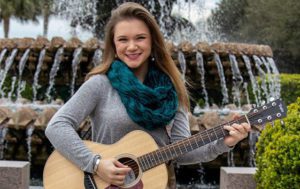 Alisa Ljungquist plays guitar in front of a fountain downtown Charleston