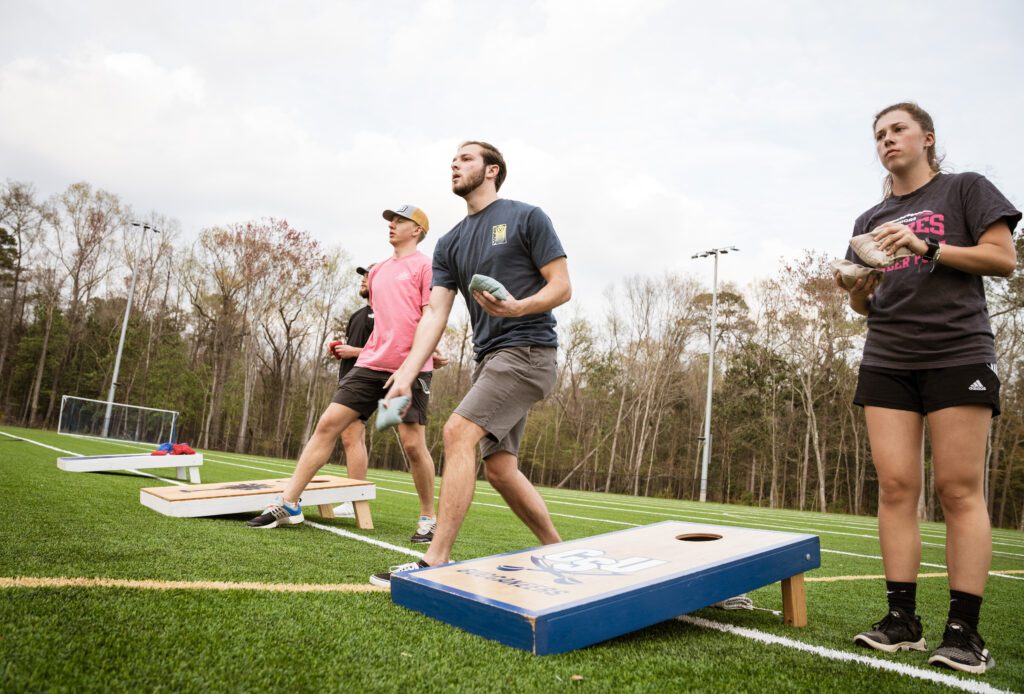 Students playing a game. Each side there is a box with a hole and students goal is to throw the sandbags in the hole.